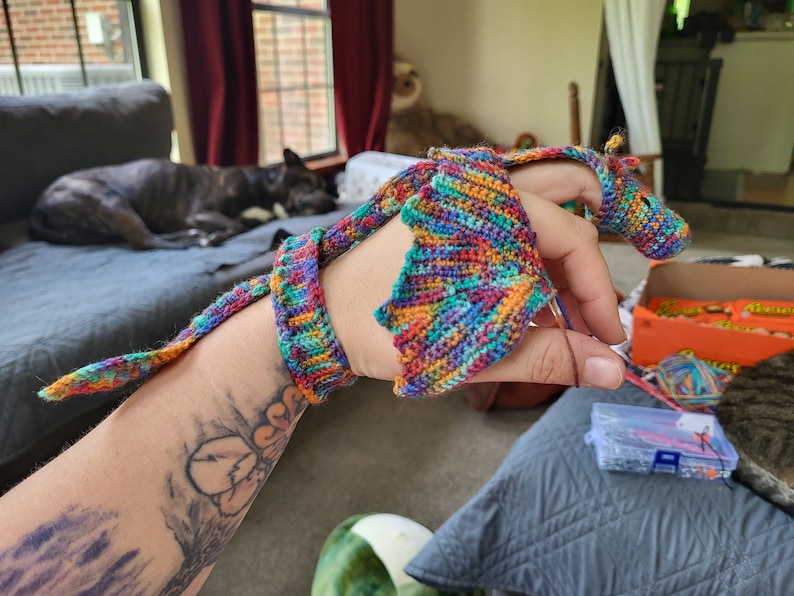 Peut inclure: Une personne est en train de crocheter un dragon color&eacute; avec une longue queue. Le dragon est fait de plusieurs couleurs, dont le rouge, l'orange, le jaune, le vert, le bleu et le violet.