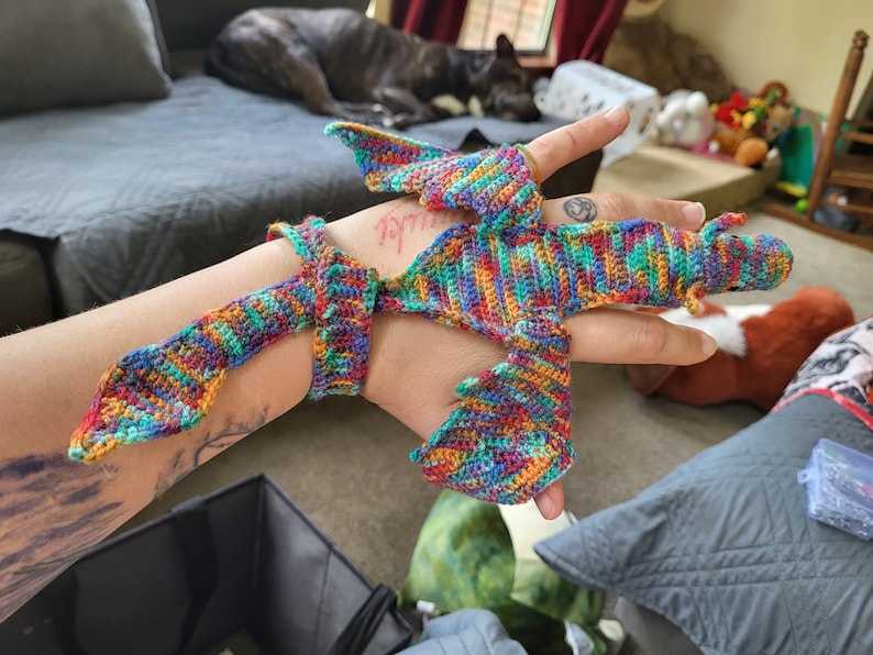 Peut inclure: Un doigt de marionnette de dragon en crochet color&eacute; avec une longue queue et des ailes. La marionnette est faite avec une vari&eacute;t&eacute; de couleurs, dont le rouge, l'orange, le jaune, le vert, le bleu et le violet.