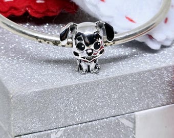 May include: Silver charm featuring a cartoon Dalmatian dog with black spots. The charm is on a silver bracelet with a red and white background.