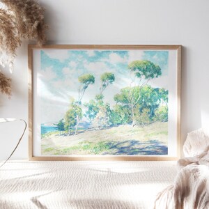 May include: A framed watercolor painting of a landscape with a group of trees on a grassy hill. The sky is blue with white clouds and the sun is shining. The trees are green and have long branches. The grass is green and there is a body of water in the distance.