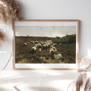 May include: A framed painting depicting a flock of sheep walking across a grassy field. The sheep are white and the field is a muted green and brown. The sky is a light blue with some clouds. The painting is in a simple wooden frame.