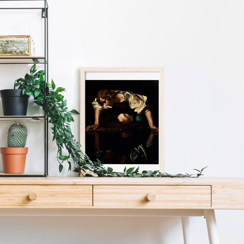 May include: A framed print of a painting depicting a young person kneeling by a body of water, looking at their reflection. The person is wearing a white shirt and blue pants. The painting is set against a dark background.