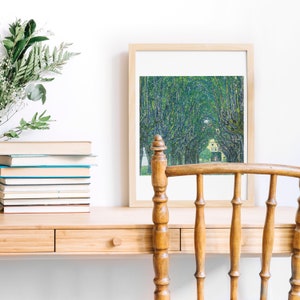 May include: A framed print of a painting depicting a tree-lined path with a house in the distance. The print is hanging on a wall above a wooden desk with a chair.