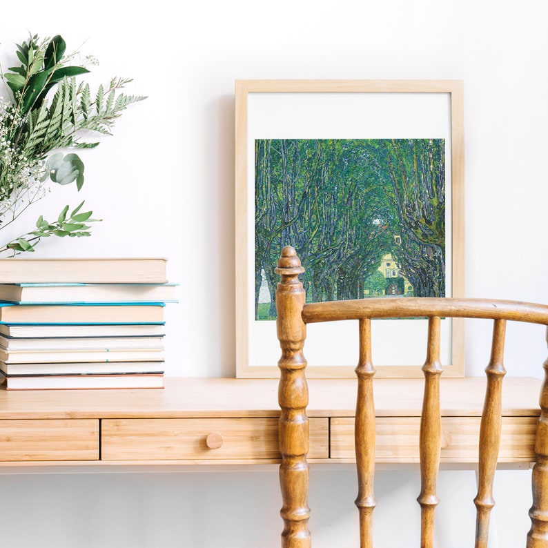 May include: A framed print of a painting depicting a tree-lined path with a house in the distance. The print is hanging on a wall above a wooden desk with a chair.