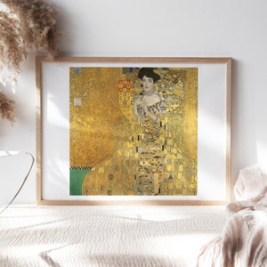 May include: A framed print of a painting depicting a woman in a gold dress with a geometric pattern. The background is a gold leaf design.