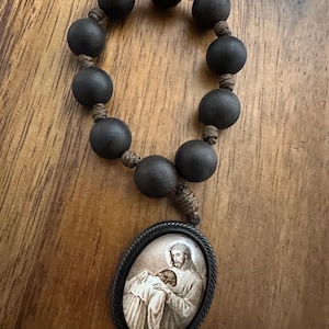 May include: A brown wooden rosary with a black oval pendant featuring a religious image of Jesus comforting a person.