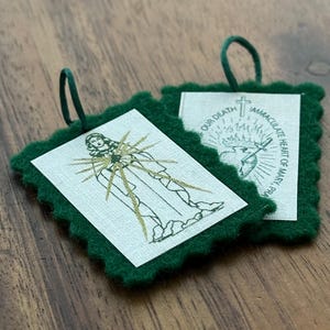 May include: Two green felt squares with scalloped edges, each featuring a religious image. The first square shows a woman with a heart and rays of light. The second square shows a heart with a sword and a cross. The text on the second square reads "Our Death Immaculate Heart of Mary".