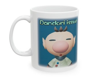 Peut inclure: Une tasse en céramique blanche avec un fond bleu et un personnage de dessin animé avec un gros nez rose. Le texte "Danclori issue" est imprimé en vert sur la tasse.