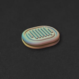 Op de afbeelding: Een ovaalvormige knoop met een verloop van zachte pastelkleuren, waaronder blauw, geel en roze. Het bovenoppervlak heeft een reeks verhoogde, parallelle horizontale ribbels en de knoop heeft een duidelijk gelaagd randprofiel.