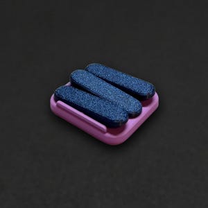 May include: A small square lavender base with rounded corners supports three parallel, elongated, dark blue glittery bars. The bars are arranged diagonally across the surface of the lavender base, creating a textured and layered appearance.