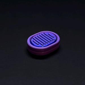 Puede incluir: Objeto ovalado impreso en 3D con una parte superior azul estriada y una base morada. El objeto tiene un diseño en capas, con la parte superior azul dentro de un marco morado. El fondo es negro liso.