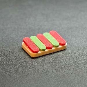 May include: A small, wooden xylophone toy with five keys. The keys alternate between red and green, and are set on a light brown base. The toy is set against a dark gray background.
