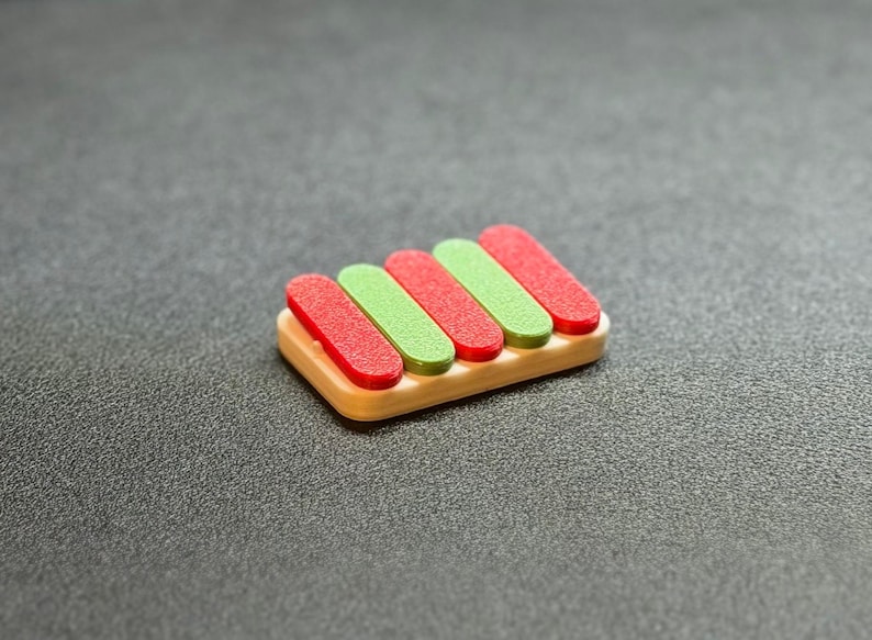 May include: A small, wooden xylophone toy with five keys. The keys alternate between red and green, and are set on a light brown base. The toy is set against a dark gray background.