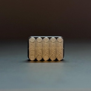 May include: A rectangular, black and beige object with six cylindrical compartments. The compartments are beige and have a textured, patterned design. The object is on a dark gray surface.