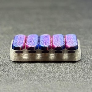 May include: A small, rectangular, silver-colored object with five colorful, rectangular, raised sections. The raised sections have a gradient of pink, blue, and purple hues. The object is likely a decorative or functional item.