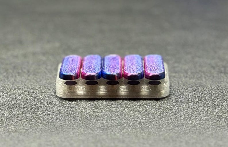 May include: A small, rectangular, silver-colored object with five colorful, rectangular, raised sections. The raised sections have a gradient of pink, blue, and purple hues. The object is likely a decorative or functional item.