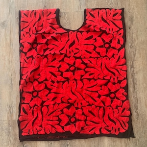 Pode incluir: Top vermelho bordado com um design floral sobre um fundo preto. O top tem um decote largo e mangas curtas.