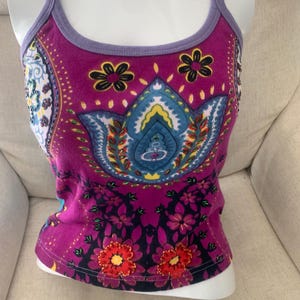 Peut inclure: Un débardeur magenta avec des bordures violet clair sur les bretelles et l'encolure. L'avant présente un grand motif floral central inspiré du cachemire bleu et jaune, accentué par de petites fleurs noires et rouges près de l'ourlet.
