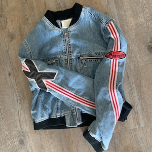 May include: A blue denim jacket with red and white stripes on the sleeves and a black patch that says "Manager" on the right sleeve.