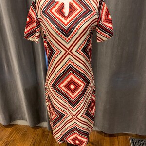Pode incluir: Vestido vintage até ao joelho com um padrão geométrico. O vestido apresenta um fundo creme com formas de diamante vermelhas e azul marinho e linhas pontilhadas. Tem mangas curtas e um pequeno decote em forma de fechadura.