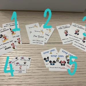May include: White cards with Disney character graphics and text. Mickey and Minnie Mouse are featured on the cards, along with phrases like "Pixie Dusted" and "Have a Magical Day!" The cards are scattered on a wooden surface.