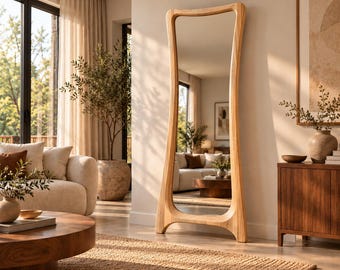 May include: A tall, floor-standing mirror featuring a light-toned, natural wood frame with a distinctively curved, organic shape. The frame is wider at the base and tapers slightly toward the top, providing a stable, arched structure for the glass.