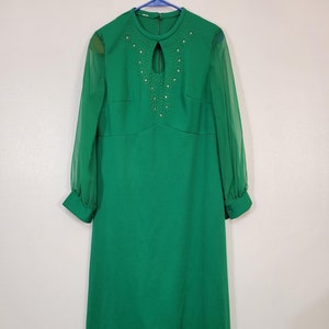May include: A long green dress with sheer sleeves and a jeweled neckline. The dress has a keyhole opening at the neckline and is made of a smooth fabric.