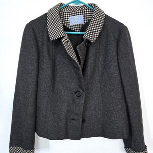 May include: A dark gray blazer with a black and white checkered collar and cuffs. The jacket has a three-button closure and is hanging on a blue hanger. The label inside the jacket reads "Jacara Winter Wear".