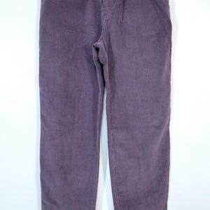May include: A pair of purple corduroy pants with a high waist and a straight leg. The pants have a button and zipper closure, front pockets, and belt loops. The corduroy fabric has vertical ridges.