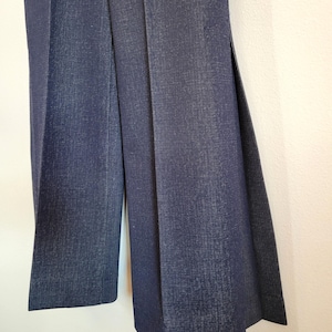 May include: Dark blue denim pants with wide legs. The pants have a high waist and a textured appearance. The fabric appears to be a medium weight denim, suitable for various seasons.