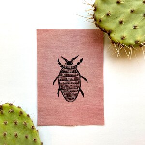 May include: A pink fabric patch with a black and white illustration of a bug. The bug has a segmented body and six legs.