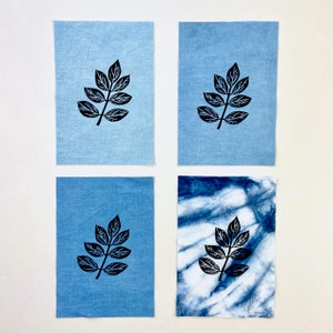 May include: Four fabric squares with a black leaf print. Two squares are a solid light blue, one is a darker blue with a tie-dye pattern, and the last is a light blue with a white tie-dye pattern.