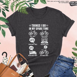May include: Dark heather grey t-shirt with a white graphic that says "Things I do in my spare time" and lists activities related to bicycles. The activities include: ride bikes, look at bikes, think about bikes, research bikes, dream about bikes, and talk about bikes.
