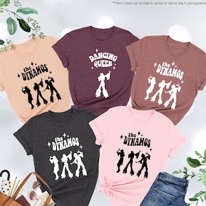 May include: Five t-shirts with different designs. The shirts are in various colors, including pink, peach, maroon, dark grey, and heather grey. The designs feature the text "the DYNAMOS" and "DANCING QUEEN" with a silhouette of a group of people dancing in the 70s style.