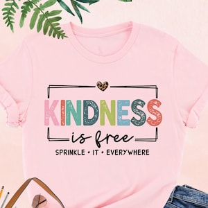 May include: Pink t-shirt with the text "KINDNESS is free - SPRINKLE IT EVERYWHERE" in colorful letters. The shirt has a small heart with leopard print on the top left corner.