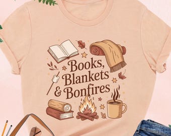 May include: Heather peach t-shirt with the text "Books, Blankets & Bonfires" and illustrations of a book, blanket, bonfire, and coffee mug. The shirt is paired with blue jeans, a brown purse, and black heels.