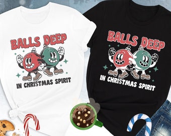 May include: Two t-shirts with a Christmas-themed design. The white t-shirt has the text "Balls Deep in Christmas Spirit" and the black t-shirt has the text "Balls Deep in Christmas Spirit". Both shirts feature a cartoon image of two Christmas baubles with faces.