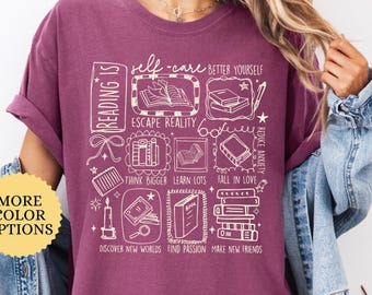 May include: Berry-colored t-shirt with white graphic text and illustrations related to reading and self-care. The design includes books, candles, and phrases like "Escape Reality" and "Find Passion." A button on the left says "More Color Options."