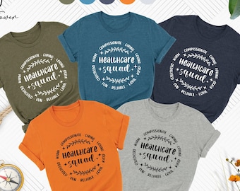 May include: Five t-shirts in different colors with a white graphic design that says "Healthcare +squad." The graphic design is a circle with a wreath of leaves around the text. The t-shirts are heather olive, heather deep teal, heather navy, orange, and athletic heather.