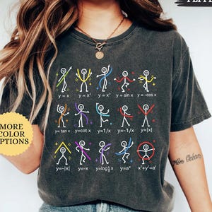 May include: A charcoal gray t-shirt featuring a graphic of fifteen white stick figures performing various poses that correspond to mathematical function equations printed in white text below each figure, including y=x, y=x², and x²+y²=a².