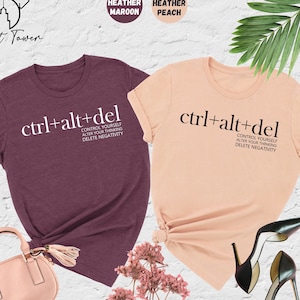 May include: Two t-shirts with the text "ctrl+alt+del" and the phrase "Control yourself, alter your thinking, delete negativity" printed on them. The shirts are in heather maroon and heather peach colors.