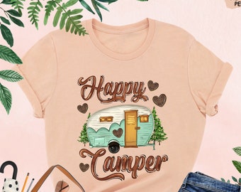 May include: A peach colored t-shirt with the text "Happy Camper" in brown lettering. A vintage camper van with brown trim and teal accents is pictured above the text. The camper van has brown hearts on the side.