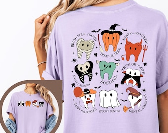 Op de afbeelding: Een orchideekleurig t-shirt met een afbeelding op de achterkant van negen cartoon-tanden verkleed in verschillende Halloween-kostuums, waaronder een mummie, pompoen, duivel en spook. De tekst bevat zinnen zoals Brush Your Tooth, Dental Boo Crew en Spooky Dentist.