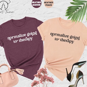 May include: Two t-shirts with the text "normalize going to therapy" in white and black lettering on a heather maroon and heather peach background.