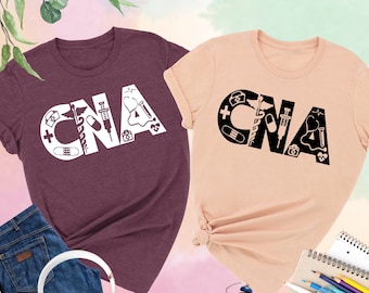 May include: Two t-shirts with the letters CNA in white and black, made up of medical symbols. The shirts are heather maroon and heather peach.