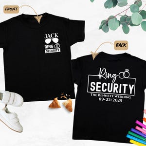 May include: Two black t-shirts with white text. The front shirt says "Jack Ring Security" with sunglasses and wedding rings. The back shirt says "Ring Security" with wedding rings and "The Bennett Wedding 09-22-2025".