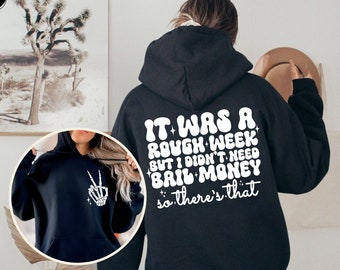 Peut inclure: Sweat-shirt à capuche noir avec un imprimé graphique blanc qui dit "It was a rough week but I didn't need bail money so there's that".
