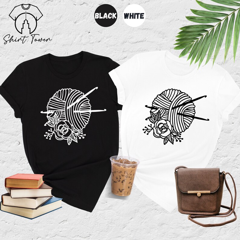 Pode incluir: Duas camisetas com um gr&aacute;fico de um novelo de l&atilde; com agulhas de tric&ocirc; e flores. As camisetas s&atilde;o preta e branca. O texto "Shirt Tower" &eacute; vis&iacute;vel no canto superior esquerdo da imagem.
