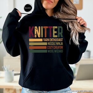 May include: Black hooded sweatshirt with a vintage-style graphic that says "Knitter" and lists the words "Yarn Enthusiast", "Needle Ninja", "Cozy Creator", and "Wool Wizard".
