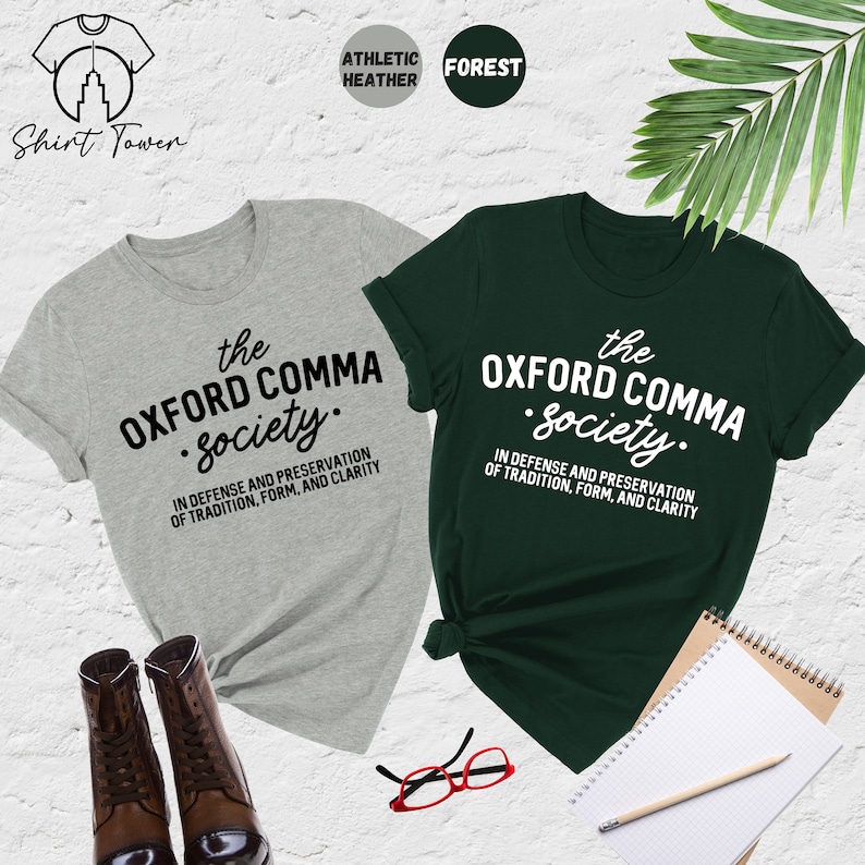 Op de afbeelding: Twee T-shirts met de tekst "the Oxford comma society." in zwart en wit. De tekst staat op een grijs en een groen T-shirt. De tekst luidt "In verdediging en behoud van traditie, vorm en duidelijkheid."